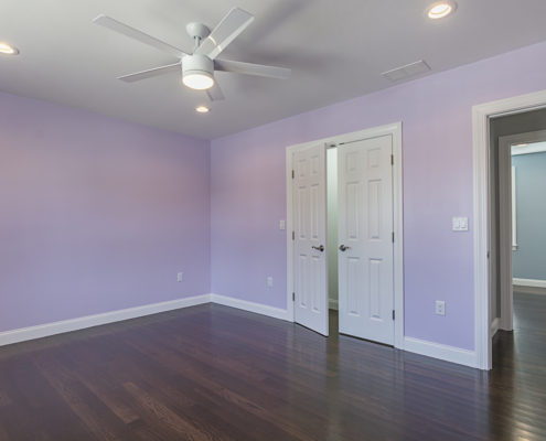 Designer bedroom with light purple walls, double doors and dark hardwood floors.