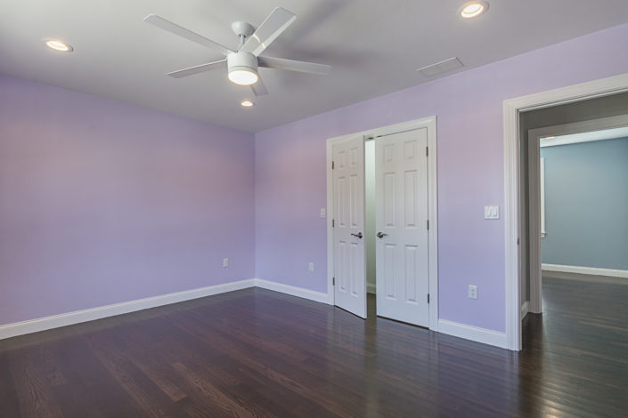 Designer bedroom with light purple walls, double doors and dark hardwood floors.